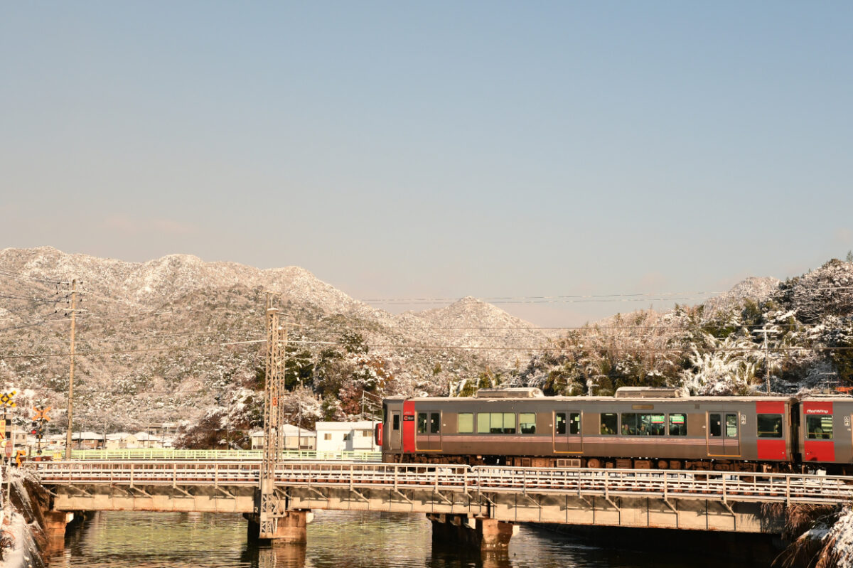 雪山をバックに永慶寺川を渡る227系