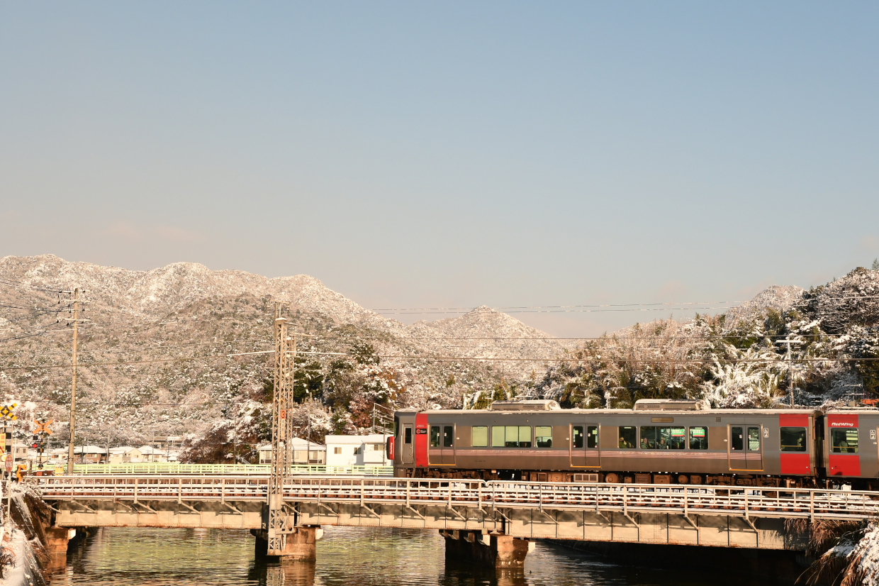 雪山をバックに永慶寺川を渡る227系